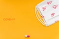 Red capsule and a white mask with red pattern on a bright yellow background, top view. Royalty Free Stock Photo