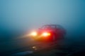 red car with bright headlights piercing through thick morning fog Royalty Free Stock Photo