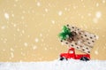 Red car carrying a gift box on a yellow background. Snowing. Christmas and New Years concept. Copy space