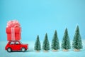 Red car carrying on roof a gift box and Christmas tree on a blue background. Christmas holiday concept Royalty Free Stock Photo