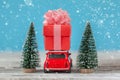 Red car carrying on roof a gift box  and Christmas tree on a blue background. Christmas holiday concept Royalty Free Stock Photo