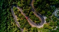 A red car driving down a winding road in the middle of a forest Royalty Free Stock Photo
