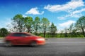 A red car driving fast on the countryside road with trees and bushes against a blue sky with clouds Royalty Free Stock Photo