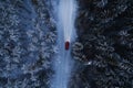 Red car driving on winter mountain road at night time. Beautiful aerial view with the trees covered in snow. Royalty Free Stock Photo