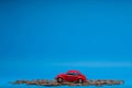 Red car figurine placed on top of a heap of golden coins, on blue background