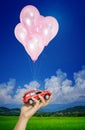 Red car in hand woman hanging on many balloons flying over blue sky. Automobile asset concept. Royalty Free Stock Photo