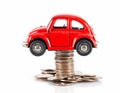 Red car model jacked by a stack of dollar coins on white background