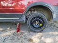 A red car with one of its tires replaced with a spare tire. The car was lifted with a jack