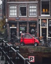 A red car parked outside an Amsterdam cafe on an autumn day.