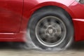 Red car racing spinning wheel burns rubber on floor. Royalty Free Stock Photo