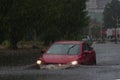 Red car rides in heavy rain on a flooded road