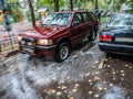 Red car rides in the yard on a wet road in the rain . Beautiful splashes of water from under the wheels. Royalty Free Stock Photo