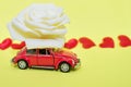 Red car with rose flower on yellow background with red hearts. Red retro car delivers flowers. Valentine, postcard March 8 Royalty Free Stock Photo