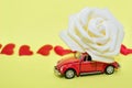 Red car with rose flower on yellow background with red hearts. Red retro car delivers flowers. Valentine, postcard March 8 Royalty Free Stock Photo