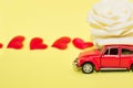 Red car with rose flower on yellow background with red hearts. Red retro car delivers flowers. Valentine, postcard March 8 Royalty Free Stock Photo