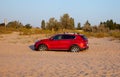 The red car skidded in the sand on the beach. The wheels are stuck in the ground. Outdoor