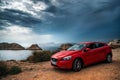 Red car Volvo v40 standing on the edge of a cliff against the stormy sky.