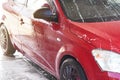 Red car washed in self serve carwash, detail on side covered with water sprayed from high pressure stream hose