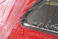 Red car washed in self serve carwash, detail on white soap foam flowing over side window and red body plates Royalty Free Stock Photo