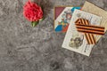 Red carnation, symbol of May 9 - St. George ribbon, old postcard and letters from the front on the gray marble of the monument.