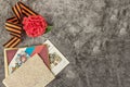 Red carnation, symbol of May 9 - St. George ribbon, old postcard and letters from the front on the gray marble of the monument.