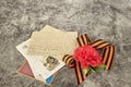 Red carnation, symbol of May 9 - St. George ribbon, old postcard and letters from the front on the gray marble of the monument.