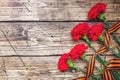 Red carnations and St. George ribbon on wooden background. Symbol may 9, victory day Copy space