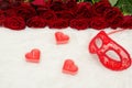 Red carnival mask and candles of heartshaped on a wooden table on a background of scarlet roses