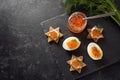 Red caviar on halved eggs and on toasted canapes in star shape with dill, preparation for a festive Christmas buffet on a dark