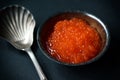 Red caviar on a plate with silver spoon on a dark background, selective focus