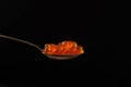 Red caviar in a silver teaspoon on a black background