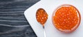 Red Caviar on a spoon and glass bowl. Salmon fish caviar. Raw seafood. Luxury food. Dark natural wooden background.