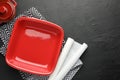 Red ceramic casseroles and baking parchment paper on black table, flat lay. Space for text Royalty Free Stock Photo