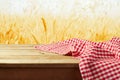 Red checked tablecloth on wooden deck table over wheat field background