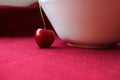 Red cherries near a white cup on a red background