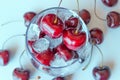 Red cherries in transparent glass bowl on light background.