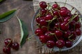 Red cherries in a transparent glass bowl on a wooden background, with green leaves of a cherry tree. Summer berries. Yummy Royalty Free Stock Photo