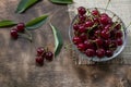 Red cherries in a transparent glass bowl on a wooden background, with green leaves of a cherry tree. Summer berries. Yummy Royalty Free Stock Photo