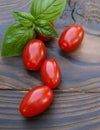 Red cherry tomatoes and basil leaves on a wooden background. Selective focus. Local products consumption concept. Healthy eating