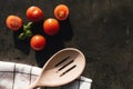 Red cherry tomatoes, green basil, wooden spoon, towel on gray background