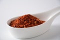 Red chili flakes in white ceramic spoon. Crushed red pepper.