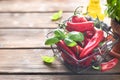 Red chili peppers with a sprig of basil in a wicker metal basket on a wooden background. Olive or vegetable oil on a Royalty Free Stock Photo