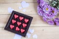 Red chocolate hearts in box and flowers on wooden table Royalty Free Stock Photo