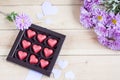 Red chocolate hearts in box and flowers on wooden table Royalty Free Stock Photo