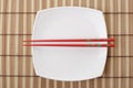 Red chopsticks and white dish on a bamboo napkin Royalty Free Stock Photo