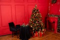 Red Christmas background with a decorated Christmas tree, an armchair, a table with candles and a fireplace Royalty Free Stock Photo