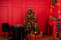 Red Christmas background with a decorated Christmas tree, an armchair, a table with candles and a fireplace Royalty Free Stock Photo