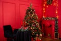 Red Christmas background with a decorated Christmas tree, an armchair, a table with candles and a fireplace Royalty Free Stock Photo