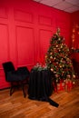 Red Christmas background with a decorated Christmas tree, an armchair, a table with candles and a fireplace Royalty Free Stock Photo