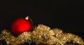 Red Christmas ball on golden garland on black background. Simple holiday decoration theme. Merry Christmas greeting card